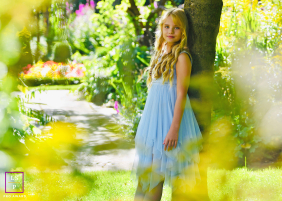 The girls blue dress serves as a cool, ethereal anchor amidst a sun-drenched sea of yellows, evoking a Pre-Raphaelite painting. The photographer masterfully uses glowing foliage to frame her striking, soulful, and magical gaze.
