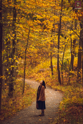 On a wooded path in Ithaca, this solitary figure pauses beneath glowing autumn leaves, completely absorbed by the season around her. The towering trees and rich golden tones give the photograph scale, quietness, and a beautifully reflective atmosphere.