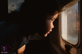 In Indre, a young girl peers through the small pet door with complete concentration, as though discovering another world beyond the glass. The warm side light and tight framing transform simple curiosity into something cinematic and deeply human.
