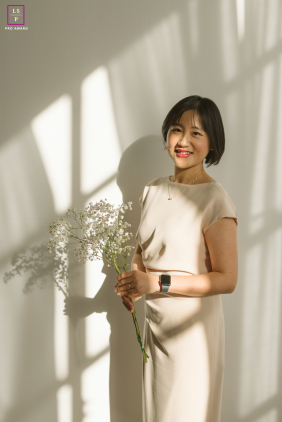In Chicago, Illinois, soft window light falls across the woman as she holds a small bouquet with quiet confidence. The clean composition and delicate shadows give the portrait simplicity, elegance, and a calm sense of grace.