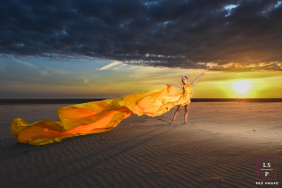 A dancer moves across the beach in a flowing orange dress, dramatically illuminated by sunset skies in St Annes, Lancashire.