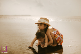 Big Sister Hugs Younger Sibling While Playing In Hilton Head Sand A big sister wraps her arms around a younger sibling as they play together in wet sand at Hilton Head, South Carolina.