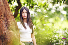 A young woman stands beside a tree, surrounded by lush green foliage during a quiet outdoor session in Blackpool, Lancashire.