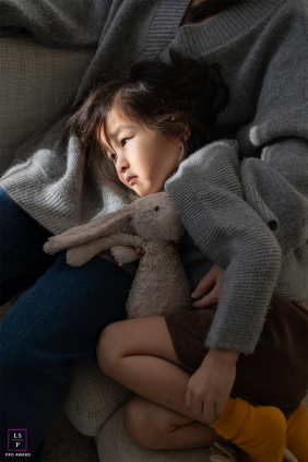 A tired young girl cuddles her stuffed animal while resting peacefully in her mother’s lap after a busy day.