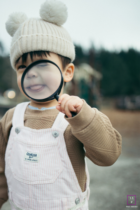 A young child playfully peers through a magnifying glass, creating a humorous view of his face during outdoor play in Oregon.