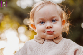 A young child gazes toward the camera with bright blue eyes, framed by warm natural light outdoors in Curitiba, Brazil.
