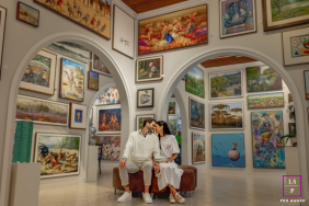 A couple shares a kiss while seated together beneath archways surrounded by colorful artwork inside a gallery in Curitiba, Brazil.