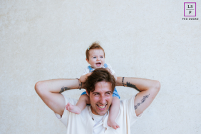 Laughing Father Carries Smiling Daughter On His Shoulders In Biarritz France A laughing father carries his smiling young daughter on his shoulders during a playful family lifestyle photography session in Biarritz, France.