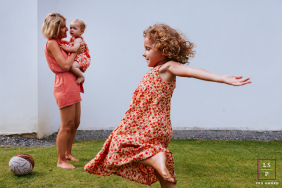 Young Girl Dances Joyfully As Mother Holds Sibling In Bayonne France A young girl dances joyfully across the lawn while her mother holds her younger sibling nearby in Bayonne, France.
