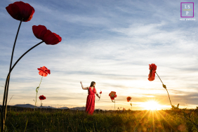A woman dances among towering red poppies in a grassy field, illuminated by warm sunset light in Bardos, Pyrénées-Atlantiques, France.