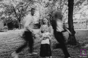 Two Girls Stand Calmly As Parents Rush Past In Loire France Two young girls stand calmly together as their parents rush past in motion during a playful family session in Loire, France.