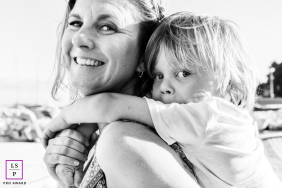 Young Boy Hugs Smiling Mother While Riding On Her Back In Carqueiranne A young boy wraps his arms tightly around his smiling mother while riding on her back at the beach in Carqueiranne, France.