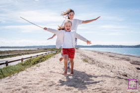 Mother And Daughter Run Joyfully Along Sandy Beach In Hyères France A mother and daughter run joyfully along the sandy beach with arms outstretched during a playful outing in Hyères, Var, France.