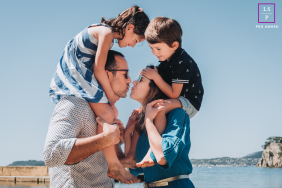 Family Of Four Shares Playful Beach Embrace In Toulon France A family of four shares a playful embrace with the children perched on their parents’ shoulders at the beach in Toulon, France.
