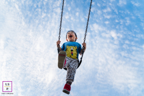 A young boy laughs joyfully while swinging high toward a bright blue sky during outdoor play in Flemington, New Jersey.