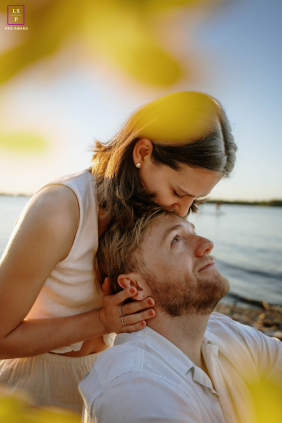 A couple shares a tender connection beside the water, framed by warm morning light during a sunrise beach session in Toronto.