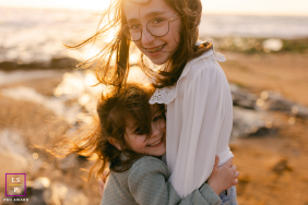 Two Sisters Embrace In Golden Light At Les Sables-d’Olonne Beach Two sisters share a warm embrace as wind sweeps through their hair during a golden-hour beach session in Les Sables-d’Olonne, France.