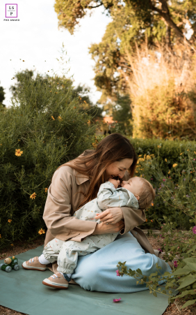 Mother Cuddles And Kisses Young Son In San Antonio Garden A mother lovingly cuddles and kisses her young son while sitting together in a garden outside a library in San Antonio, Texas.