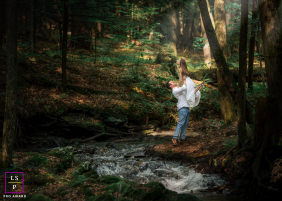 A couple embraces beside a flowing woodland stream, surrounded by lush ferns and towering trees at Saint-Gaudens National Historical Park, New Hampshire.