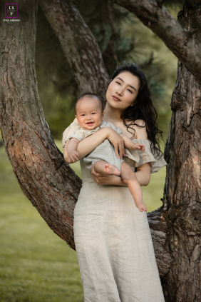 Mother Holds Smiling Baby Son Between Trees During Markham Evening A mother holds her smiling six-month-old son between trees during a peaceful outdoor family session on a quiet evening in Markham.
