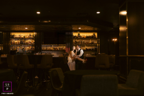 A couple shares a kiss while seated together at a bar, surrounded by the warm glow of a dimly lit lounge.