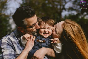 Parents Kiss Laughing Toddler During Playful Family Time In NRW Germany Parents nuzzle and kiss their laughing toddler between them while enjoying a warm, playful family time outdoors in NRW, Germany.