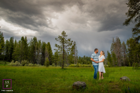 A couple stands together in a green meadow beneath dramatic storm clouds, surrounded by tall pine trees in Truckee, California.