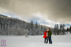 A couple shares a kiss while standing together in deep snow, surrounded by snow-covered forest and mountains in Truckee, California.