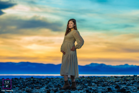 An expectant mother stands among shoreline rocks beside the lake, framed by colorful sunset skies in Tahoe City, California.