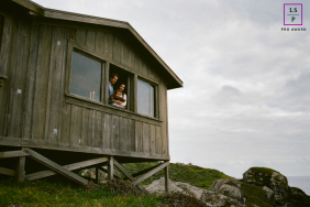 Parents Hold Young Daughter At Rustic Cabin Window In Marin California Parents hold their young daughter at an open window of a rustic wooden cabin overlooking the coastal landscape in Marin, California.