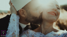 A couple shares an affectionate kiss in warm sunlight, her joyful expression highlighting their close connection outdoors in North Macedonia.