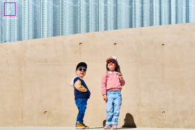 Two Children Pose Confidently In Sunglasses At Les Sables-d’Olonne France Two children wearing caps and sunglasses pose confidently together against a large concrete wall in Les Sables-d’Olonne, France.