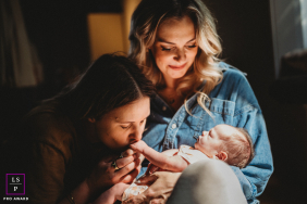 Mother Cradles Newborn As Partner Kisses Baby’s Foot In Boston A mother cradles her newborn while her partner gently kisses the baby’s tiny foot during an intimate family moment in Boston.