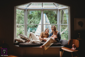 Couple Relaxes Together In Sunlit Window Seat At Home Boston A couple relaxes together in a sunlit window seat, sharing an affectionate moment while surrounded by the comforts of home in Boston.