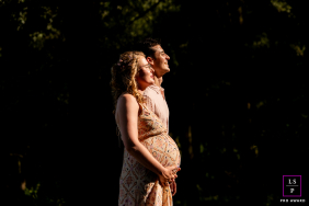 An expectant couple embraces in a beam of warm sunlight, lovingly cradling her pregnant belly in Balijbos, Zoetermeer, the Netherlands.