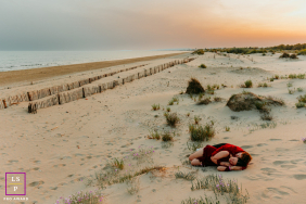 A couple cuddles together on the sand, surrounded by quiet dunes and warm evening light along the beach in La Grande-Motte, France.