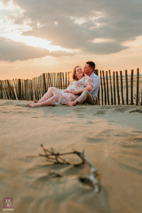 A couple relaxes together on the sand, sharing an affectionate connection beneath warm sunset skies at Plage de l’Espiguette, France.