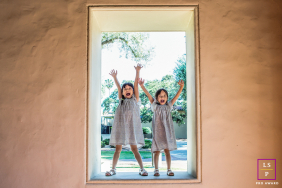 Two Young Girls Raise Their Arms Joyfully In Pasadena California Two young girls joyfully raise their arms while standing together in a sunlit doorway during a family session in Pasadena, California.