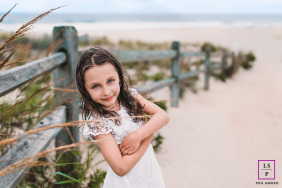 A young girl stands beside a weathered beach fence, enjoying the coastal breeze along the shoreline of Long Beach Island, New Jersey.