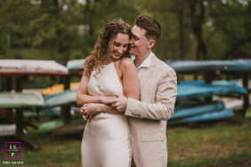 A young couple shares a tender embrace beside stacked colorful canoes and lush greenery during a relaxed session in Bergen County, New Jersey.