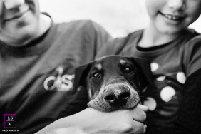A dog rests comfortably between two smiling family members, its expressive face centered during a playful pet session in San Jose, California.