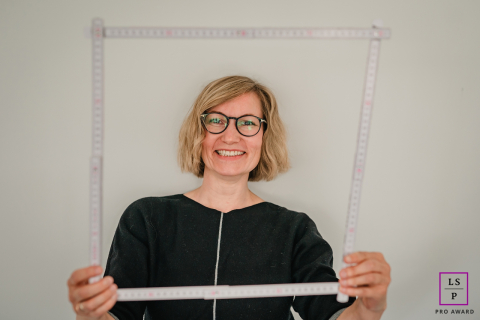A businesswoman, Sylvia Kaufmann, stands posing for a portrait on a construction site in Hagen, NRW, Germany. She confidently frames her face with measuring sticks, exuding professionalism and determination in her role.