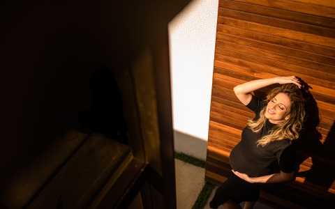 This is a lifestyle image of a pregnant woman leaning against the door of her house and receives the sunlight in Maceio