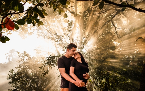 This is a lifestyle picture of man embracing his pregnant woman and in the background a strong light embraces them in Maceio, Alagoas