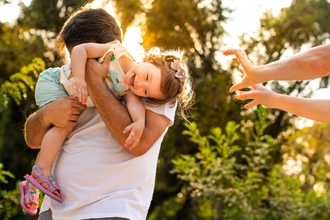 Curitiba artistic lifestyle family portrait image showing a family plays with their daughter in the park at sunset