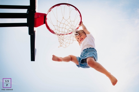 Auvergne-Rhone-Alpes young girl poses for a lifestyle image as she plays while hanging on to her daddy's basketball hoop