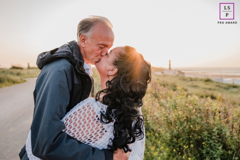 As the setting sun bathes the picturesque roadway in Breskens, Netherlands, a couple embraces, their lips locked in a tender kiss, captured in a mesmerizing lifestyle portrait