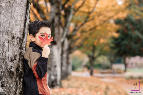 Candidly capturing curiosity and innocence in the crisp autumn air of Bothell, WA. A young boy's playful gaze peeks through a vibrant red maple leaf in this whimsical portrait.