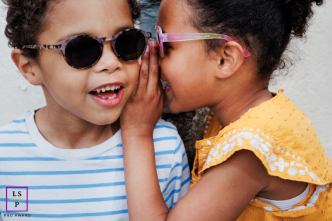 Two children keep a summer secret, sporting sunglasses, in a portrait shot by a photographer in Rennes.