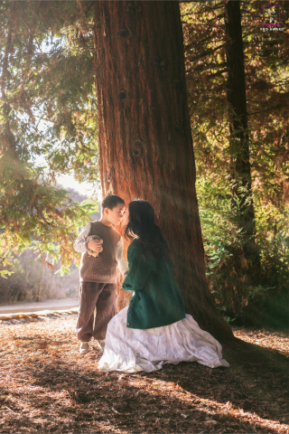 In California, a sweet scene captured in Southern Los Angeles as a mother and her young son share a tender kiss under the shade of a towering tree in a sun-kissed forest.